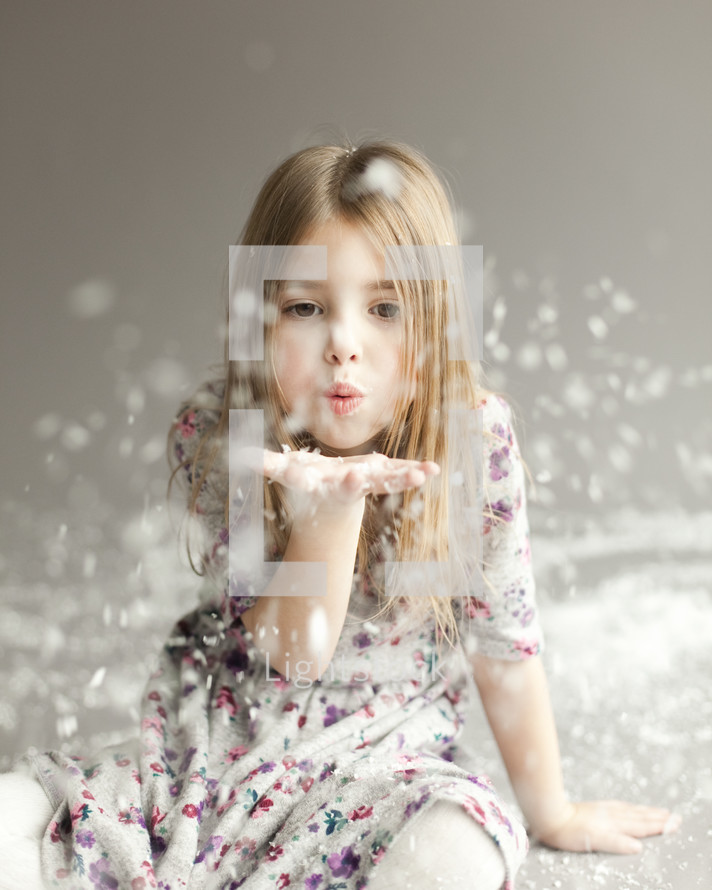 A joyful little girl blowing snow off her hand on grey backdrop