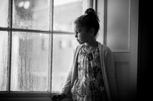 a girl sitting in a window watching the rain 