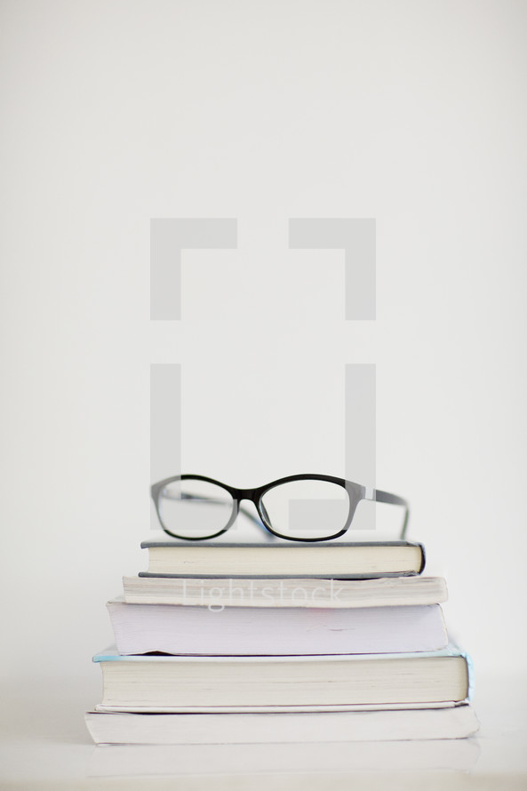 A pair of eyeglasses on top of a stack of books.