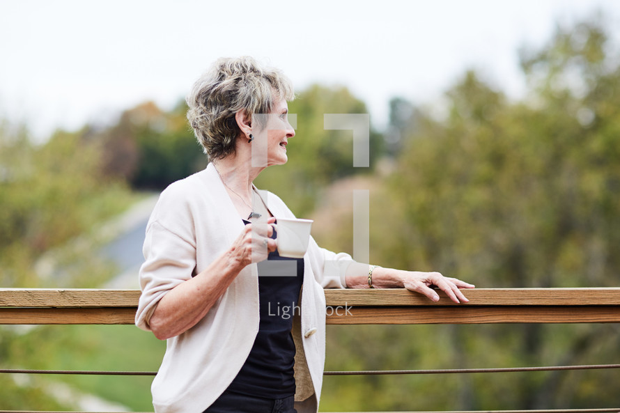 a woman standing by a railing with coffee 
