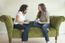 two friends drinking coffee and talking on a couch