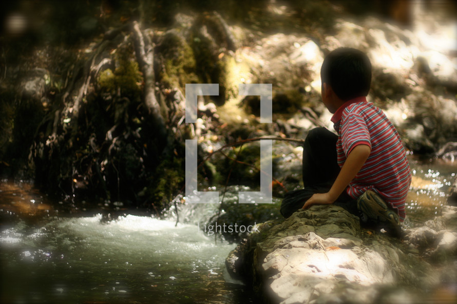 a child sitting on a rock watching water in a creek