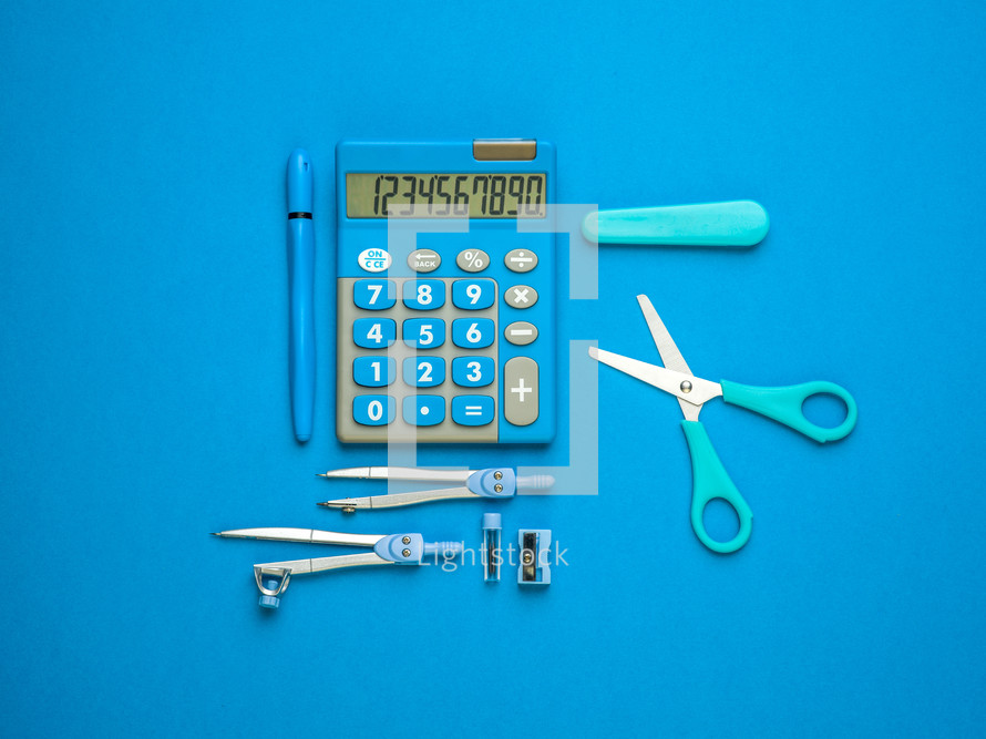 calculator, scissors, pen, compass, school supplies on blue 