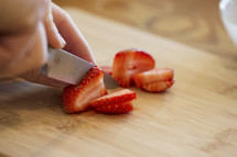 A hand slicing strawberries with a knife.