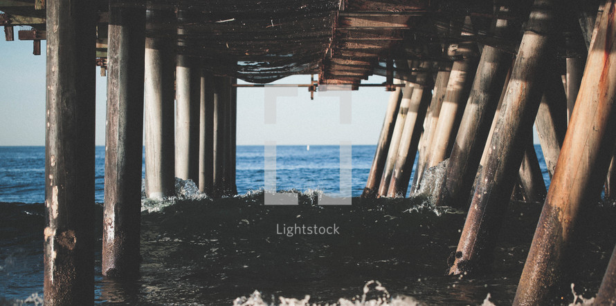 waves crashing into the pillars of a pier 