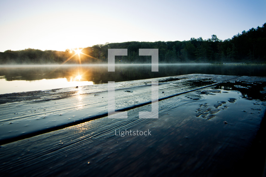 The sun rises over the trees and reflects off the dock.