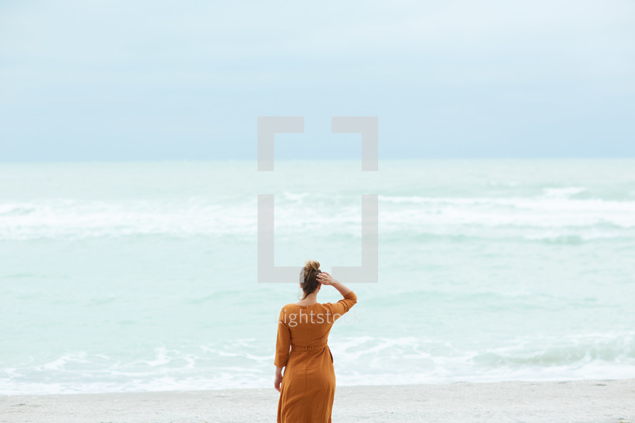 a woman standing on a beach looking out at the water 
