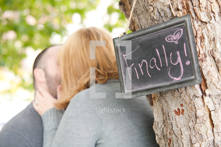 couple kissing in front of a sign with the words finally