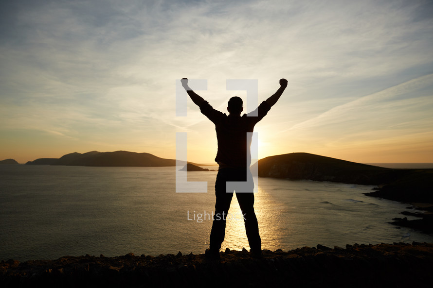 silhouette of a man with raised hands at sunset 
