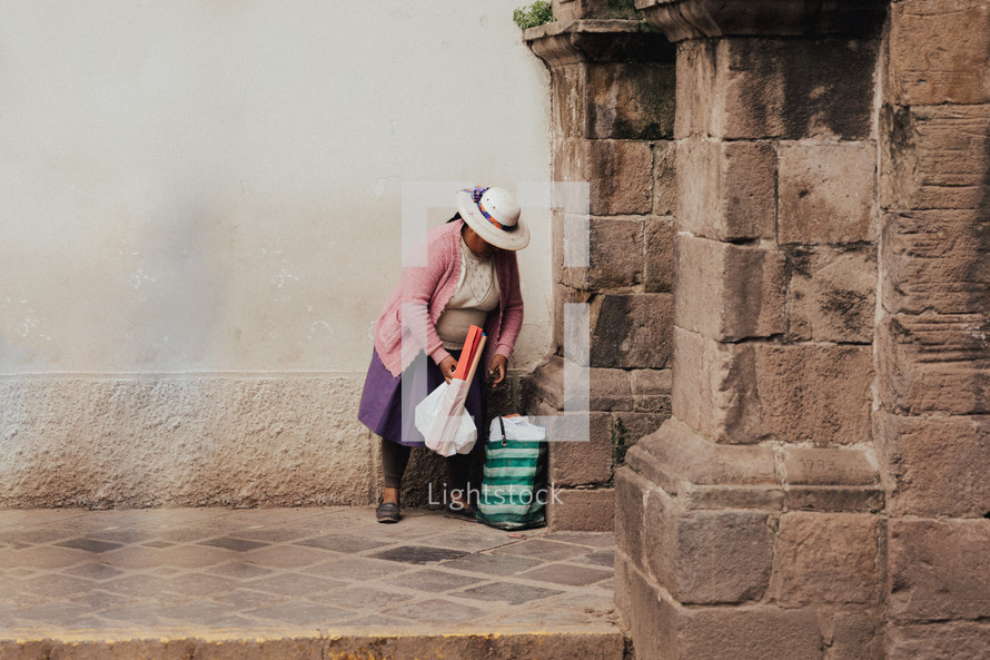 a woman gathering her bags on a stone walkway 