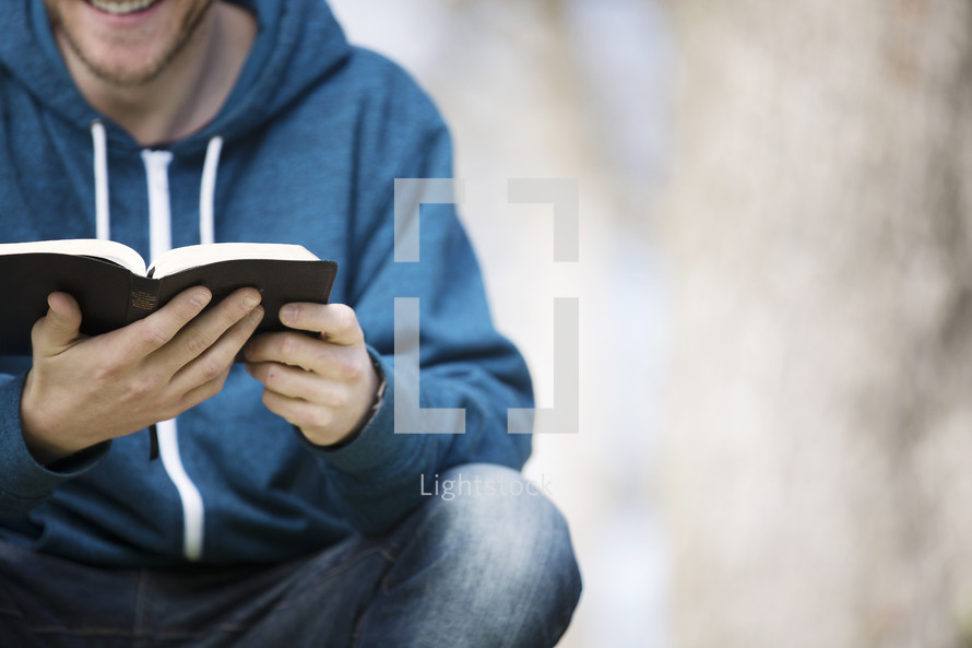 a man sitting reading a Bible outdoors 