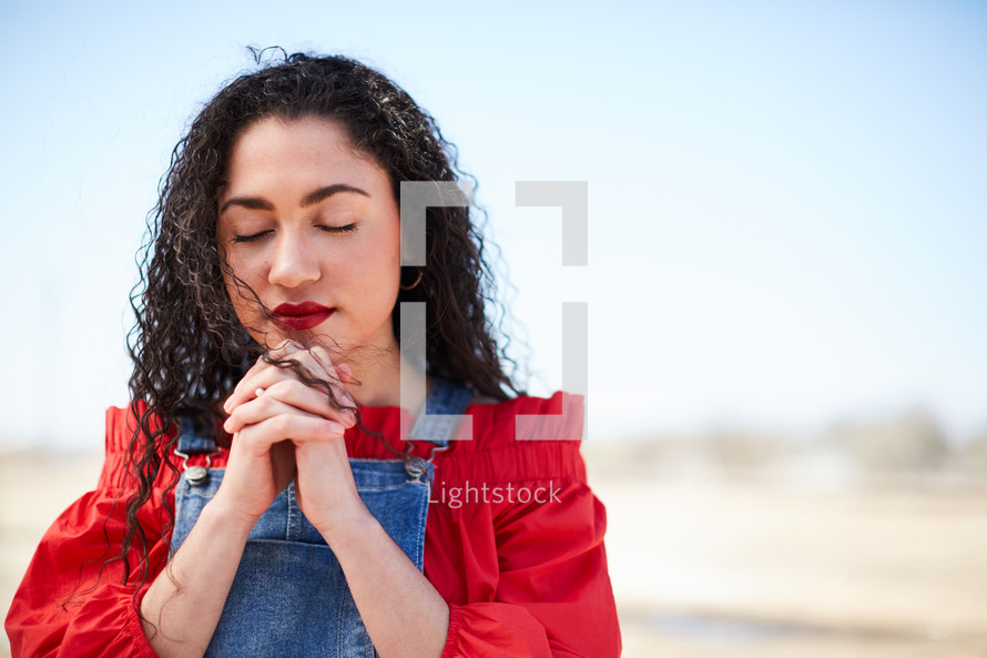portrait of a woman standing outdoors with praying hands 