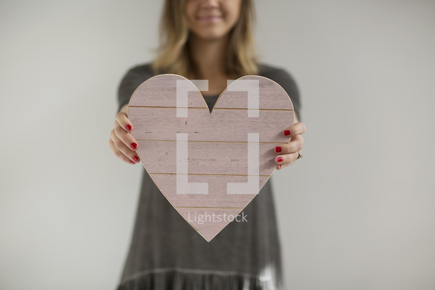 a woman holding out a wooden heart 