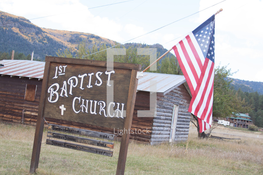 Rural church near mountains with an American flag on the sign.