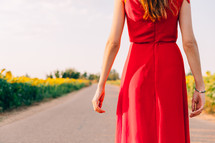 woman with red dress backwards in road with sunflowers