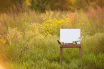easel, art supplies, and blank canvas outdoors 