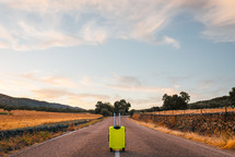 yellow suitcase on a road in the field.