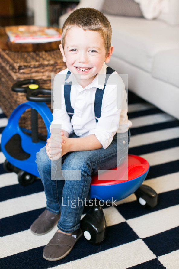 a boy child sitting on a plasma car in a living room 
