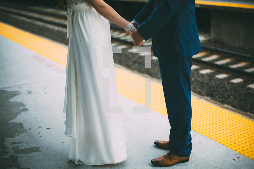 legs and torso of a bride and grooms holding hands 