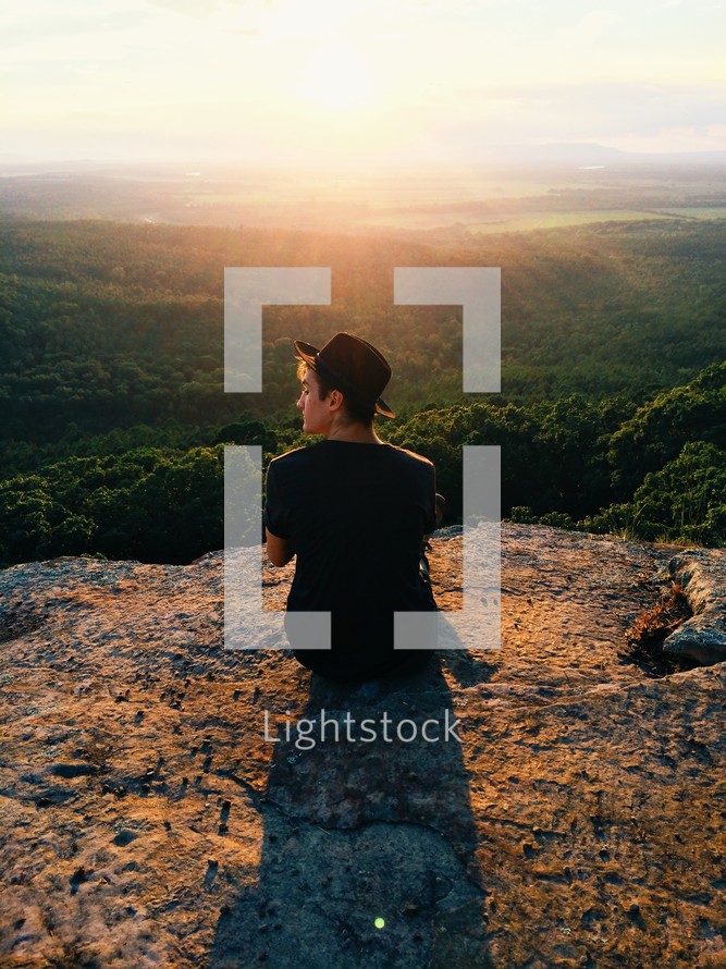 man sitting on a mountaintop at sunrise looking out 