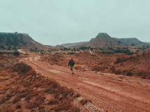 man walking down a red dirt road 