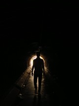 man walking towards the light in a dark tunnel 