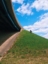 man walking up a steep hill near an overpass