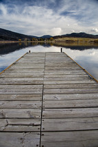 A wooden pier reaching into a placid lake.