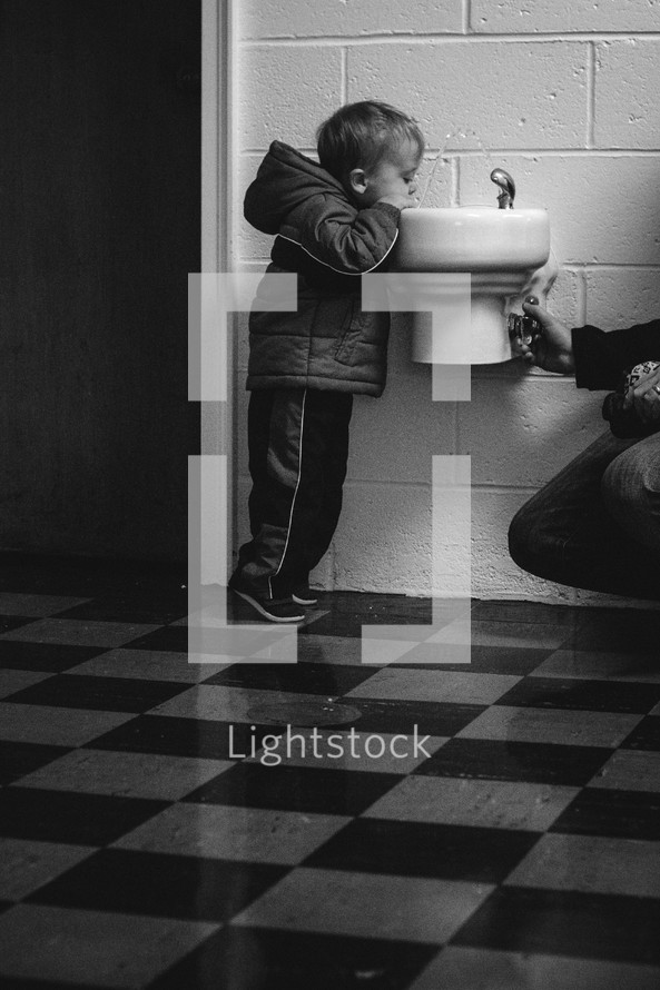 toddler boy drinking at a water fountain 