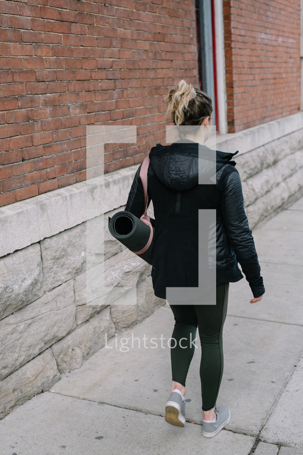 woman walking carrying a yoga mat 