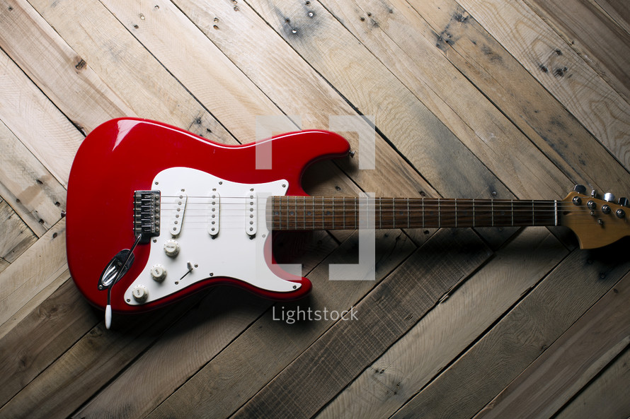 a red electric guitar on a wooden table.