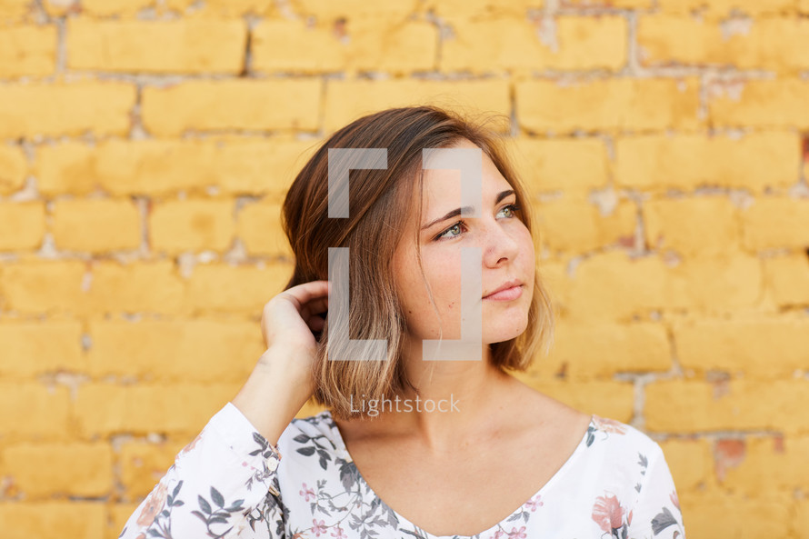 a woman standing in front of a yellow brick wall tucking her hair behind her ear 