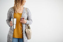 a woman standing holding a purse and listening to earbuds 