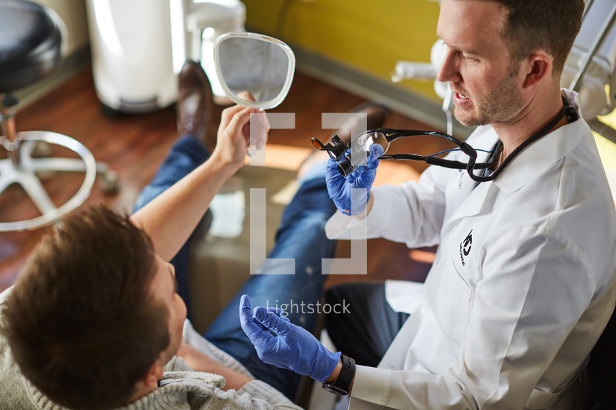 a dentist showing his patient his teeth in a mirror 