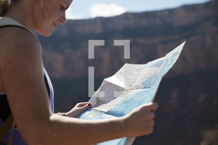 woman standing at the edge of a canyon cliff reading a map 