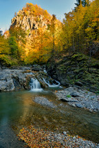 Autumn waterfall and creek woods with yellow trees foliage and rocks in forest mountain