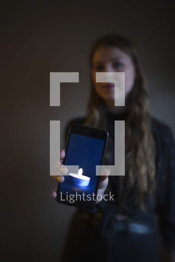 young woman holding image of candle in dark room