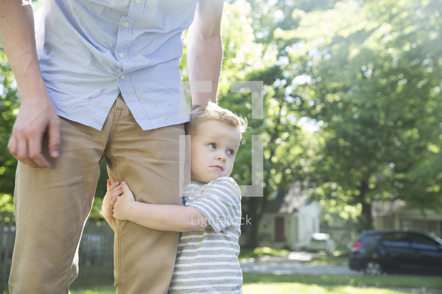 a toddler boy holding onto dad's leg