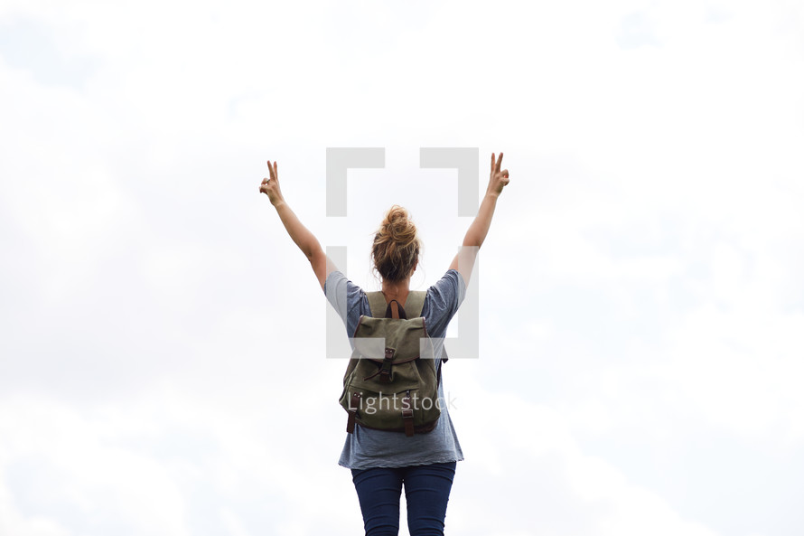 a woman with a backpack with hands raised giving peace signs 