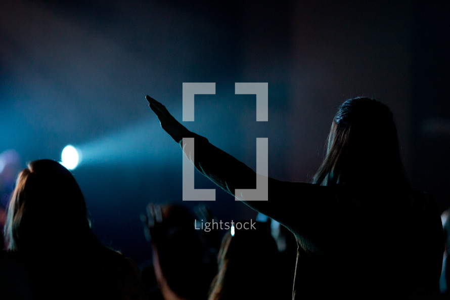 silhouettes of people in an audience at a concert with raised hands 