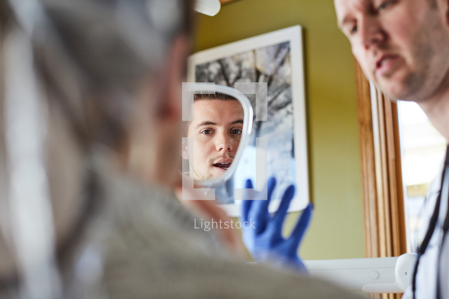 a dentist holding up a mirror so his patient can look at his teeth 
