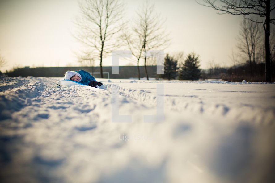 child lying on a sled in the snow