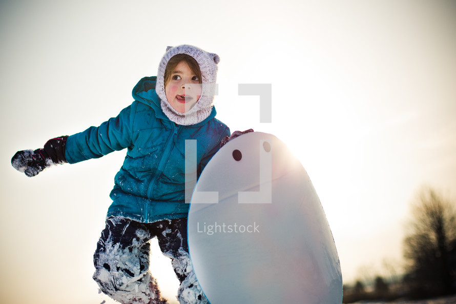 child in a winter hat and coat holding a circular sled