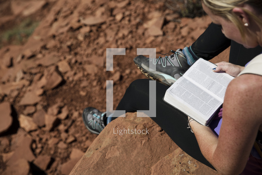 woman sitting on a rock reading a Bible in a canyon 