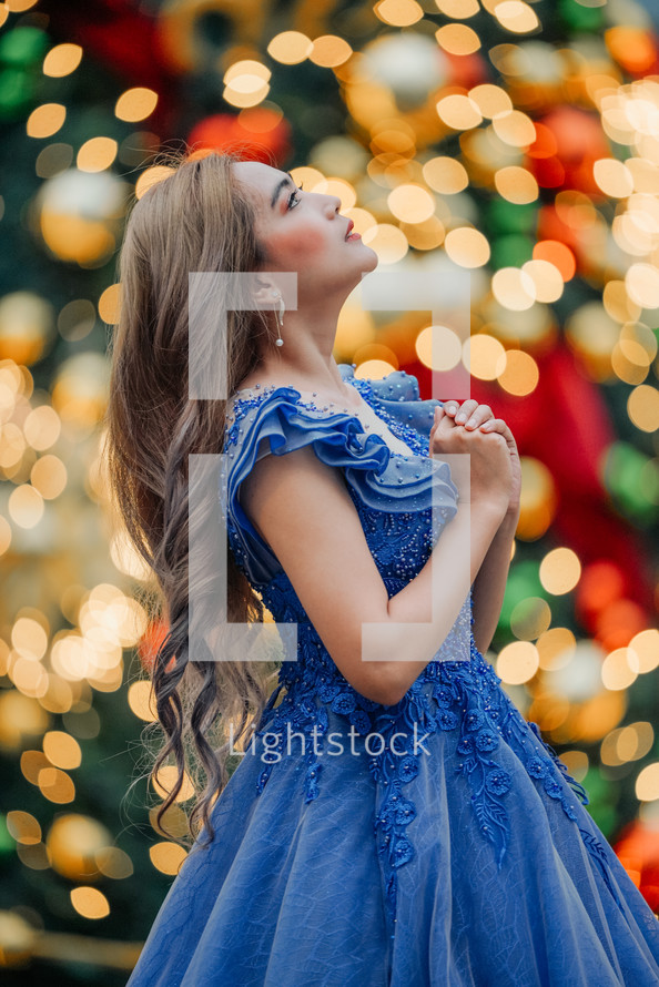 Woman looking up and praying surrounded with a bokeh of Christmas Lights