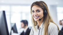 Confident female customer support representative with headset at computer in modern office.
