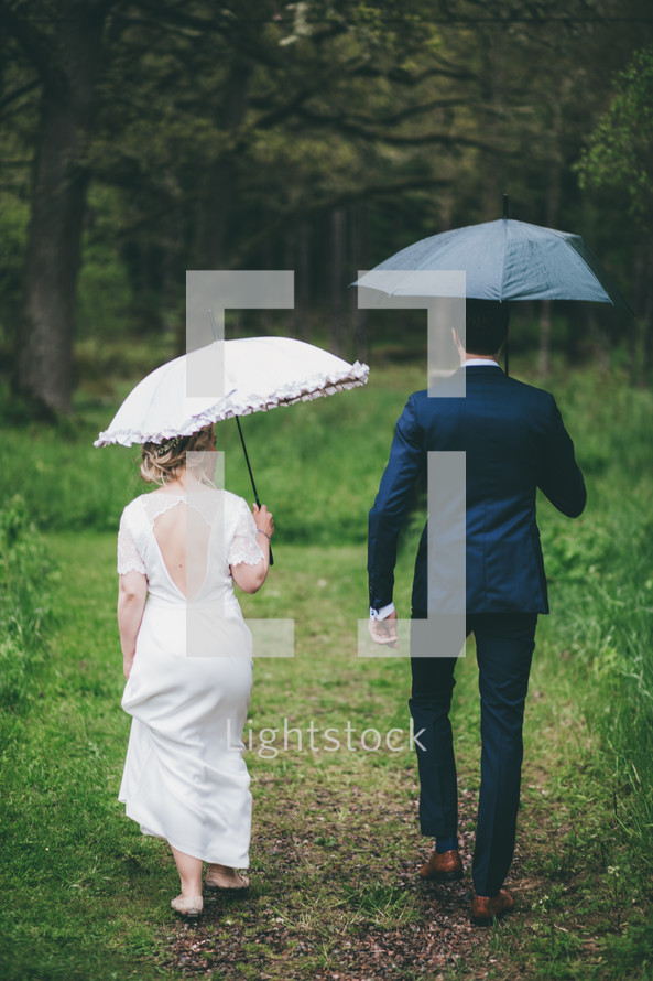 a bride and groom carrying umbrellas in the rain 