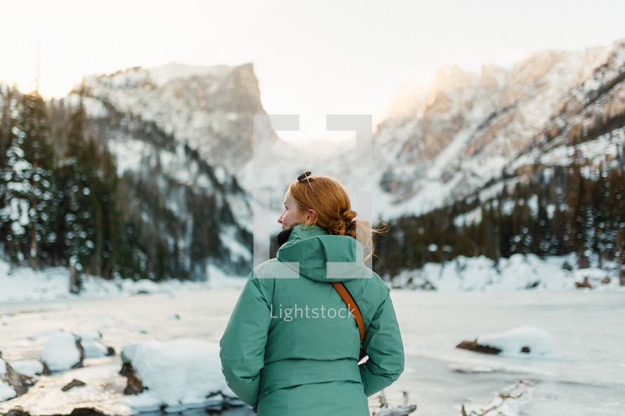 Female Hiker enjoying snowfall beside a lake in the mountains