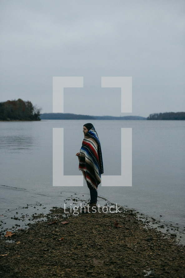 a man wrapped in a blanket standing on a lake shore 