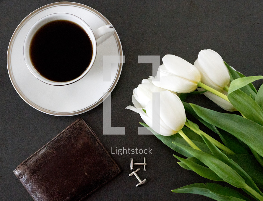 leather wallet, coffee cup and saucer, and tulips on a table 